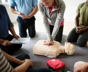 Eine Frau übt die Wiederbelebung an einer Puppe, während andere Personen zuschauen.