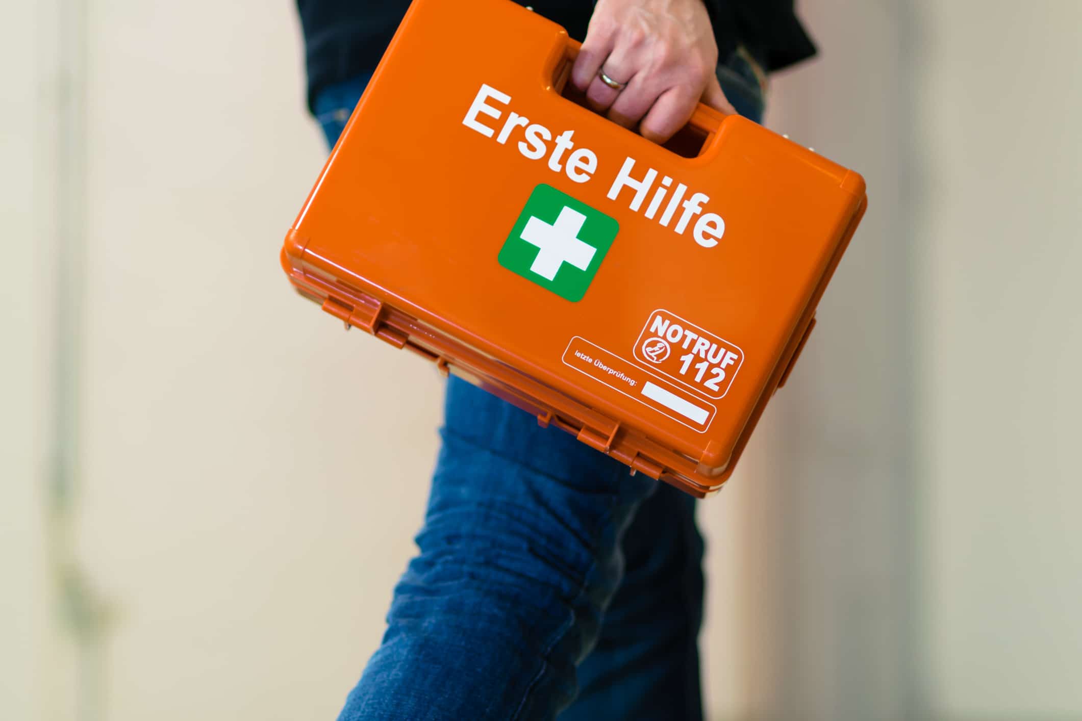 Eine Person trägt einen orangen Koffer mit dem Aufdruck „Erste Hilfe“.