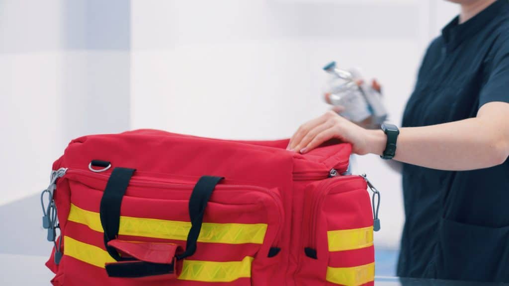 Eine Person packt eine rote Erste-Hilfe-Tasche mit gelben Streifen.