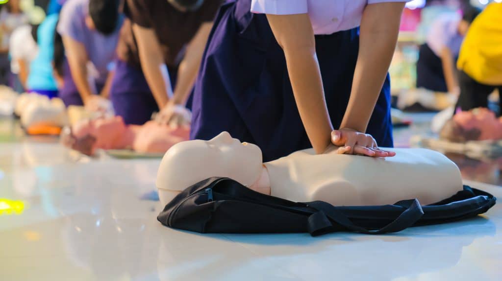 Teilnehmende üben in einem Erste-Hilfe-Kurs die Herz-Lungen-Wiederbelebung an einer CPR-Trainingspuppe auf dem Boden.
