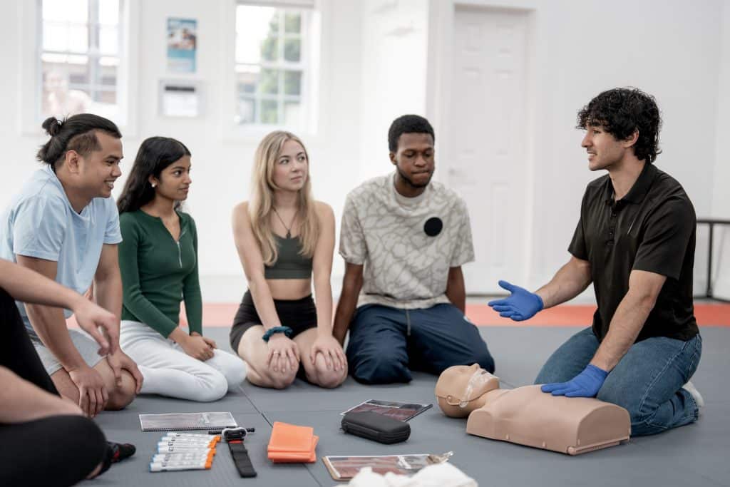Gruppenübungen in Erster Hilfe und HLW-Techniken mit dem Leiter in einem Trainingskurs.