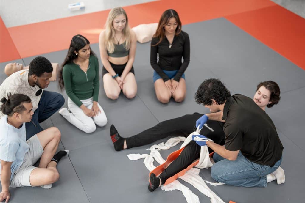 Eine Gruppe von Schülern, die während eines Erste-Hilfe-Trainings den Notfallverband üben.